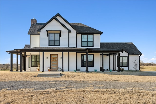 modern inspired farmhouse featuring covered porch, roof with shingles, and a chimney