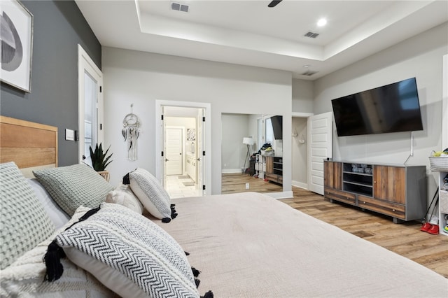 bedroom with light wood-style flooring, a raised ceiling, visible vents, and baseboards