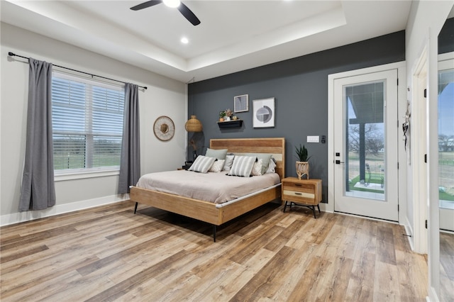 bedroom featuring access to exterior, a tray ceiling, light wood-style flooring, and baseboards