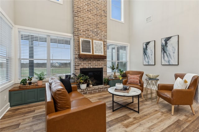 living area with light wood-style flooring, a fireplace, a towering ceiling, visible vents, and baseboards