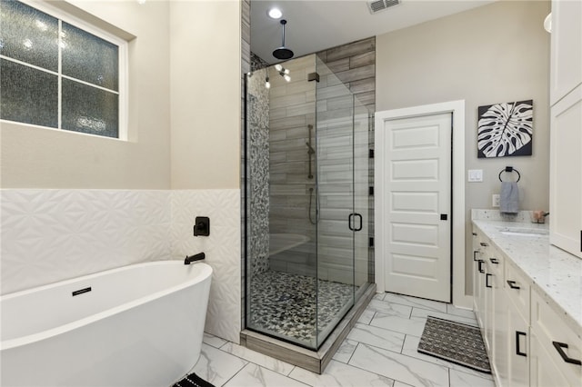 bathroom featuring marble finish floor, vanity, a freestanding tub, and a stall shower