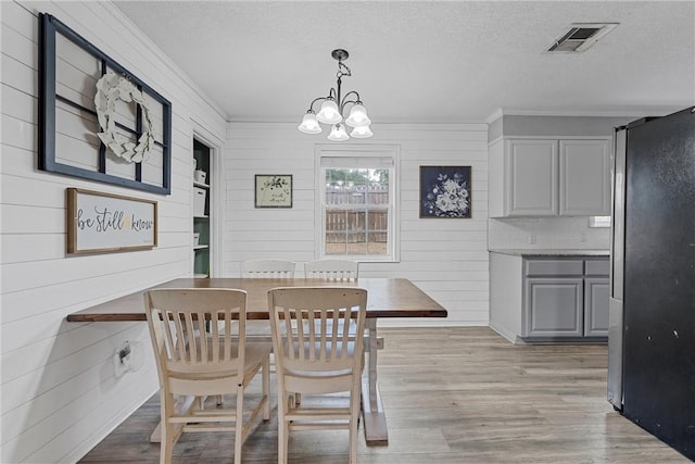 dining space with wooden walls, a textured ceiling, and light wood-type flooring