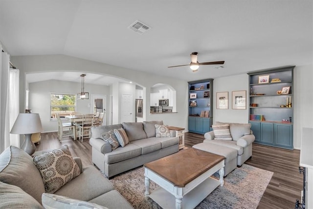 living room with built in shelves, ceiling fan, dark hardwood / wood-style floors, and vaulted ceiling