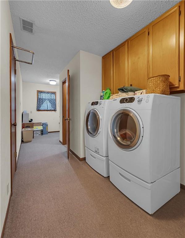 washroom featuring light carpet, washer and clothes dryer, cabinets, and a textured ceiling