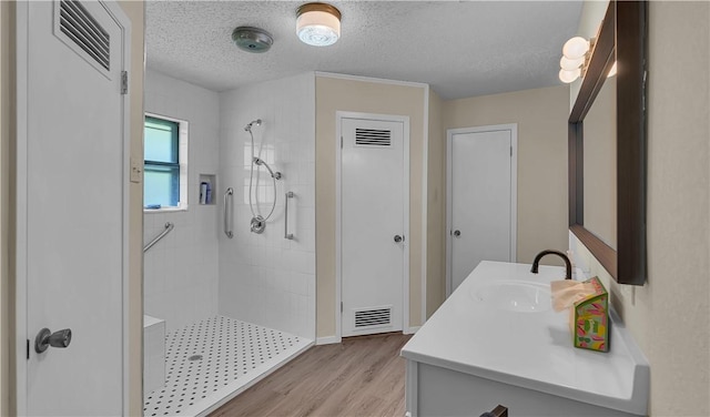 bathroom featuring vanity, wood-type flooring, a textured ceiling, and tiled shower