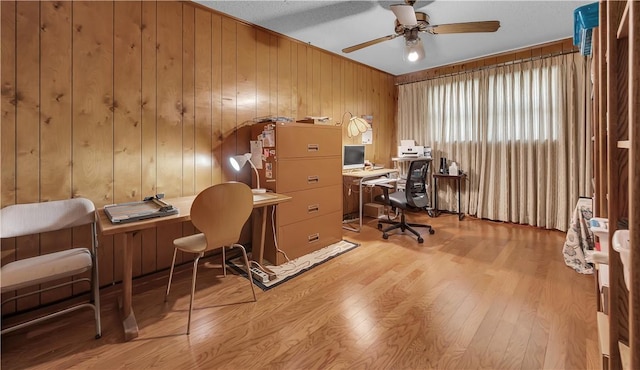 home office with light wood-type flooring, ceiling fan, and wooden walls