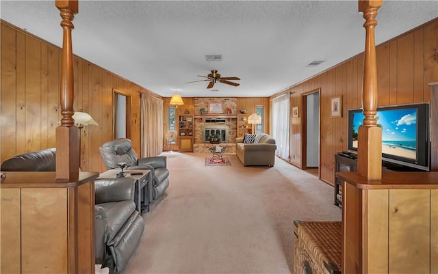 living room featuring light carpet, ceiling fan, a fireplace, and wood walls