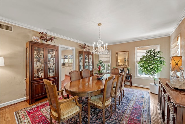 dining space with light hardwood / wood-style floors, an inviting chandelier, and ornamental molding