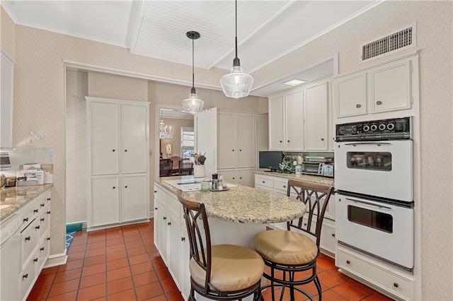 kitchen with decorative light fixtures, white cabinetry, double oven, and a kitchen island