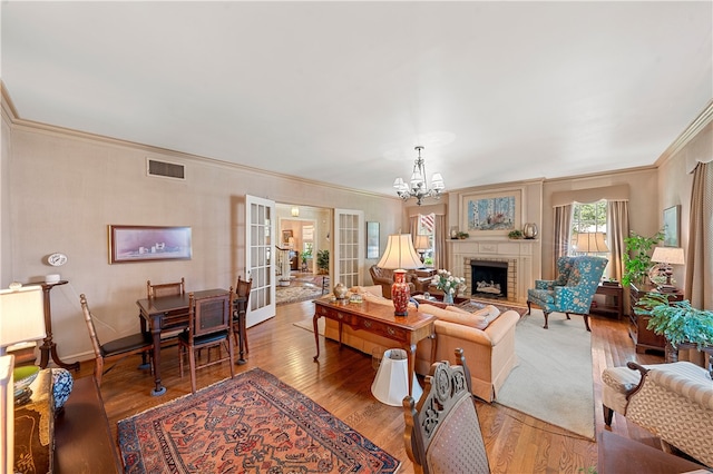 living room featuring french doors, crown molding, a brick fireplace, wood-type flooring, and a chandelier