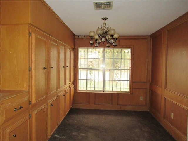 unfurnished dining area featuring a chandelier, ornamental molding, dark colored carpet, and wooden walls