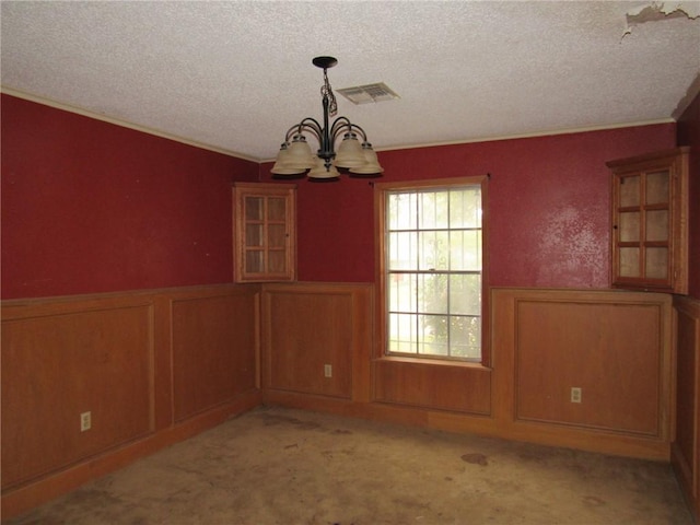 unfurnished dining area featuring crown molding, light colored carpet, a textured ceiling, and a chandelier