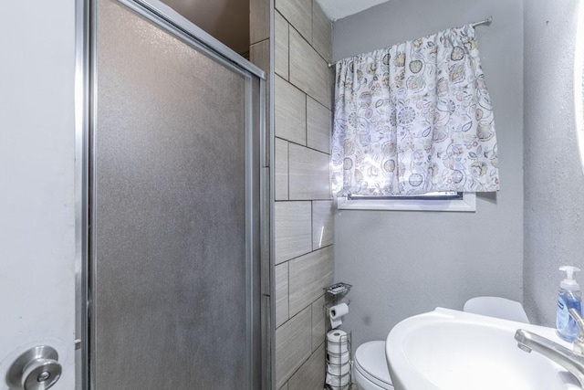 bathroom featuring toilet, a shower with door, and sink