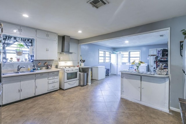 kitchen with white gas range, white cabinetry, sink, wall chimney range hood, and decorative backsplash