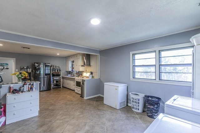 kitchen featuring crown molding, wall chimney exhaust hood, light tile patterned flooring, stainless steel appliances, and washer / clothes dryer