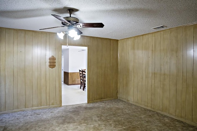 carpeted empty room with a textured ceiling, ceiling fan, and wooden walls