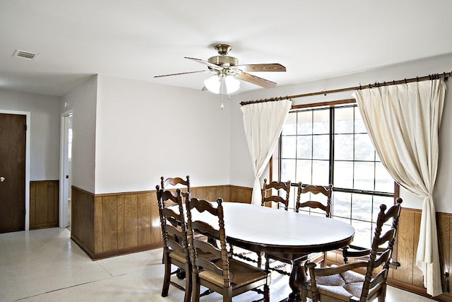 dining area featuring ceiling fan and wooden walls