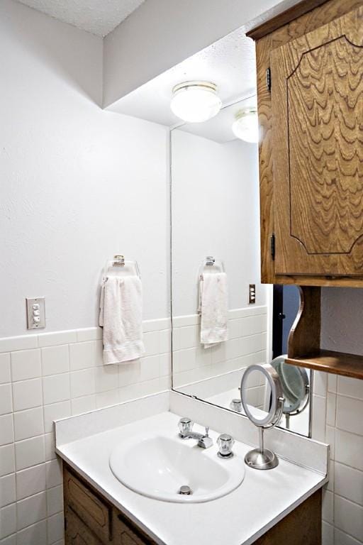 bathroom featuring a textured ceiling, vanity, and tile walls