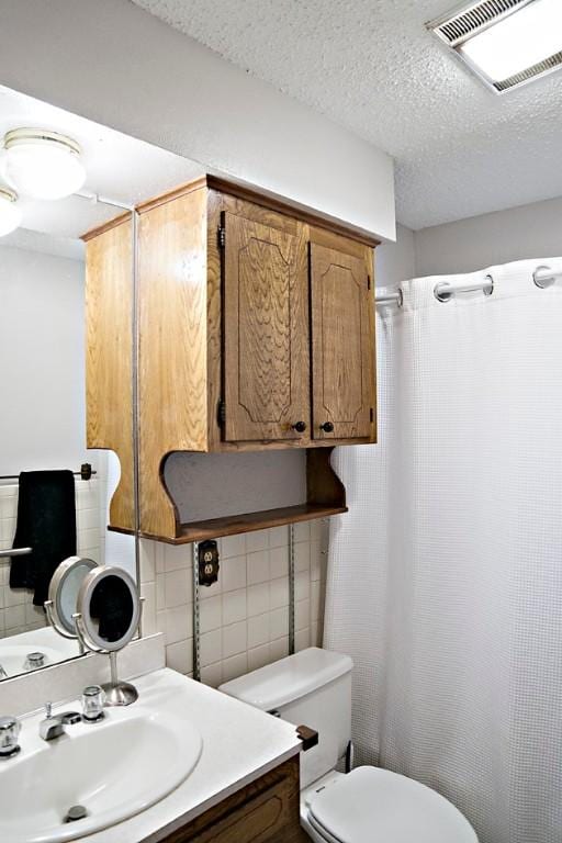 bathroom with vanity, toilet, a textured ceiling, and tasteful backsplash