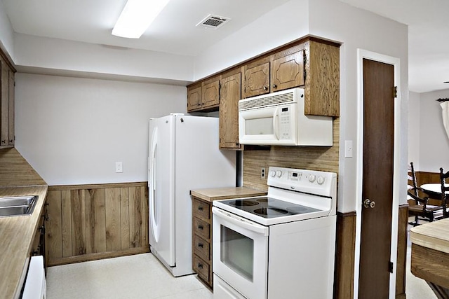 kitchen with white appliances, wooden walls, and sink