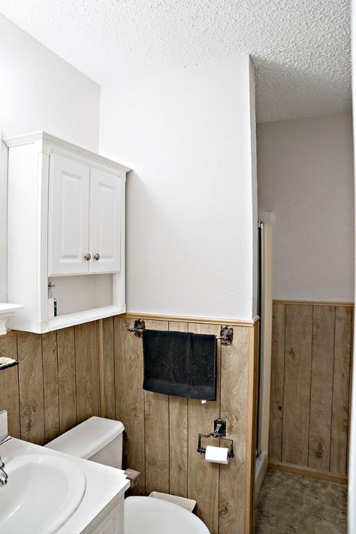 bathroom with wooden walls, vanity, a textured ceiling, and toilet