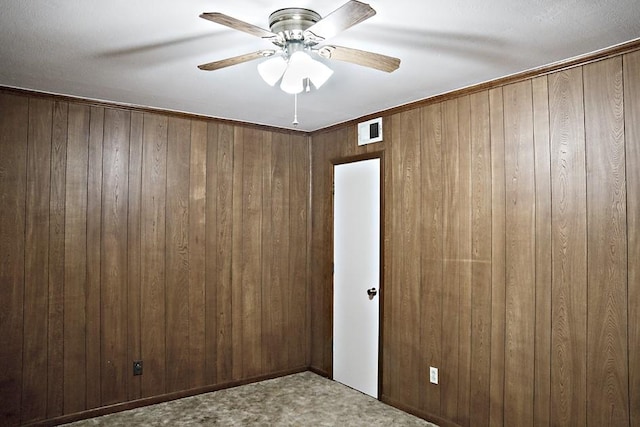 empty room featuring ceiling fan, carpet floors, and wooden walls