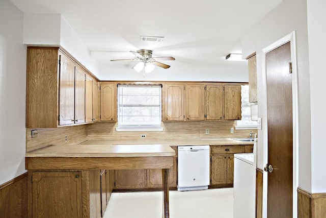 kitchen featuring kitchen peninsula, backsplash, white dishwasher, ceiling fan, and wood walls