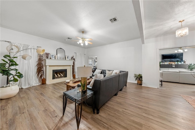 living area featuring light wood-style floors, visible vents, a fireplace, and ceiling fan with notable chandelier