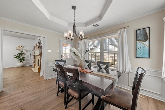 dining space featuring a wainscoted wall, light wood finished floors, a raised ceiling, and a notable chandelier