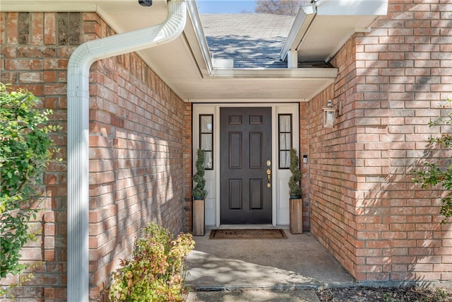 doorway to property featuring roof with shingles and brick siding