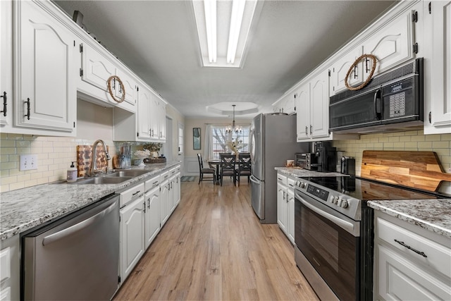 kitchen with appliances with stainless steel finishes, white cabinets, a sink, and light stone countertops