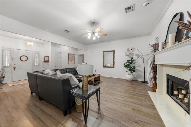 living room featuring visible vents, wood finished floors, crown molding, and a high end fireplace