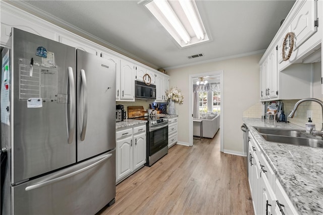 kitchen with light stone counters, a sink, white cabinets, appliances with stainless steel finishes, and crown molding