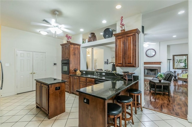 kitchen with black appliances, ceiling fan, light tile patterned floors, a kitchen island, and kitchen peninsula