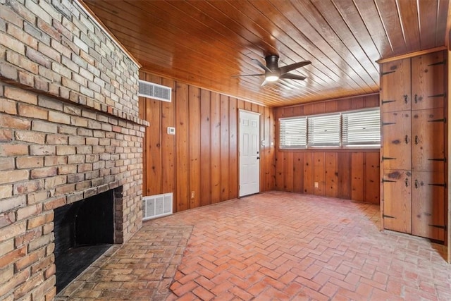 unfurnished living room featuring a fireplace, ceiling fan, wooden walls, and wood ceiling