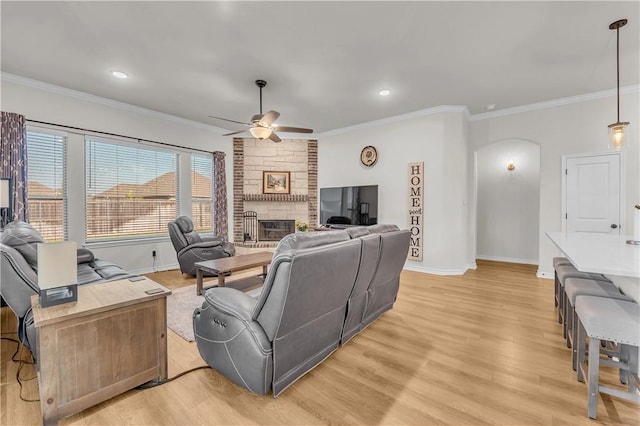 living room featuring light hardwood / wood-style floors, ceiling fan, crown molding, and a stone fireplace