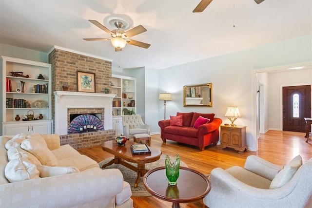 living room with ceiling fan, built in features, light wood-type flooring, and a brick fireplace