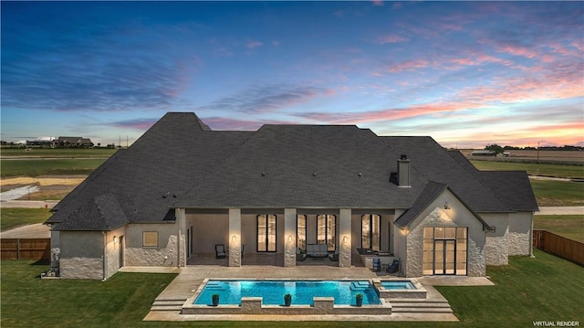 back house at dusk with a pool with hot tub, a lawn, and a patio area