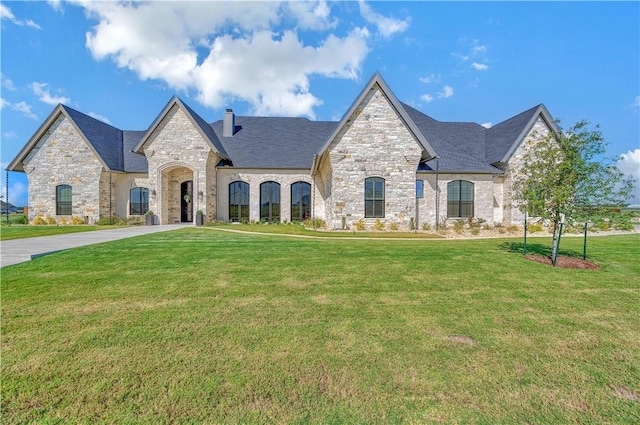 french provincial home with a chimney, concrete driveway, and a front yard