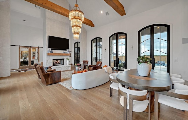 living room featuring a chandelier, high vaulted ceiling, light hardwood / wood-style flooring, beamed ceiling, and a barn door