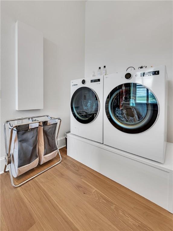 clothes washing area with hardwood / wood-style flooring and washer and dryer