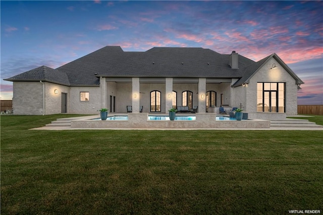 back house at dusk featuring a yard and a patio