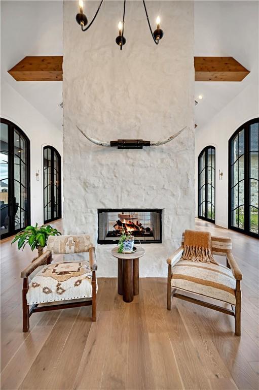 living area with a towering ceiling, light hardwood / wood-style floors, beamed ceiling, and a multi sided fireplace