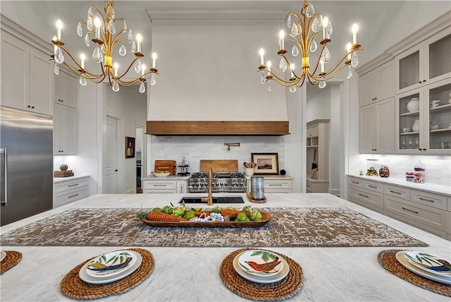 kitchen with gray cabinets, hanging light fixtures, a notable chandelier, light stone countertops, and stainless steel built in fridge