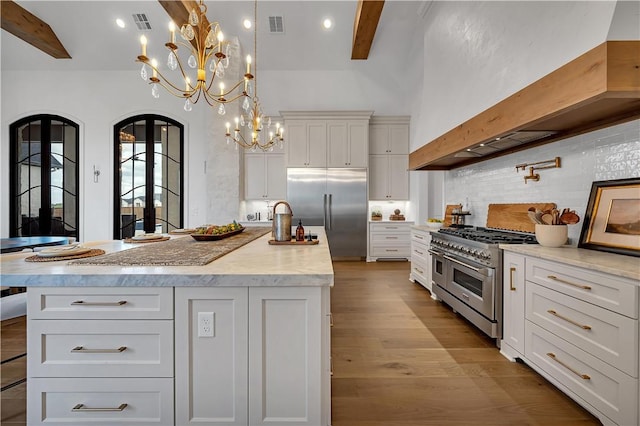 kitchen featuring high end appliances, pendant lighting, white cabinetry, and a center island with sink