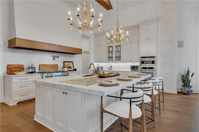 kitchen featuring double oven, decorative light fixtures, sink, white cabinets, and a center island with sink