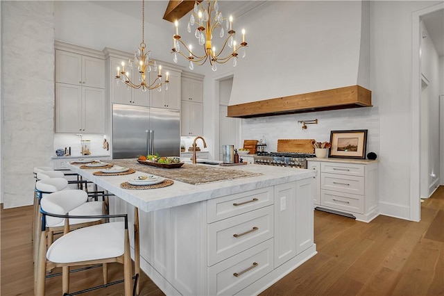 kitchen with appliances with stainless steel finishes, white cabinetry, hanging light fixtures, a kitchen island with sink, and light hardwood / wood-style floors