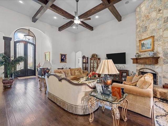 living room featuring beam ceiling, a stone fireplace, ceiling fan, and dark hardwood / wood-style floors