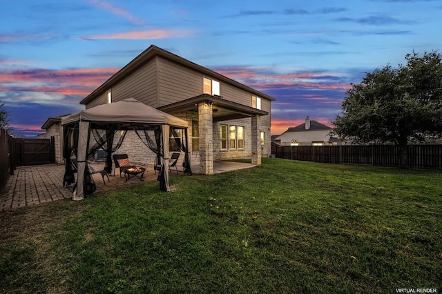 back house at dusk featuring a gazebo, a patio area, and a yard