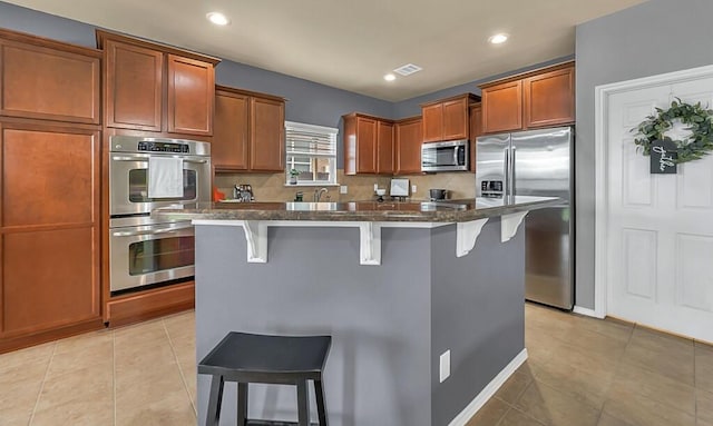 kitchen with a center island, a kitchen bar, light tile patterned floors, and stainless steel appliances